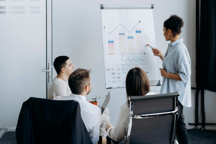 Business team in meeting with presenter discussing charts on a flip board.